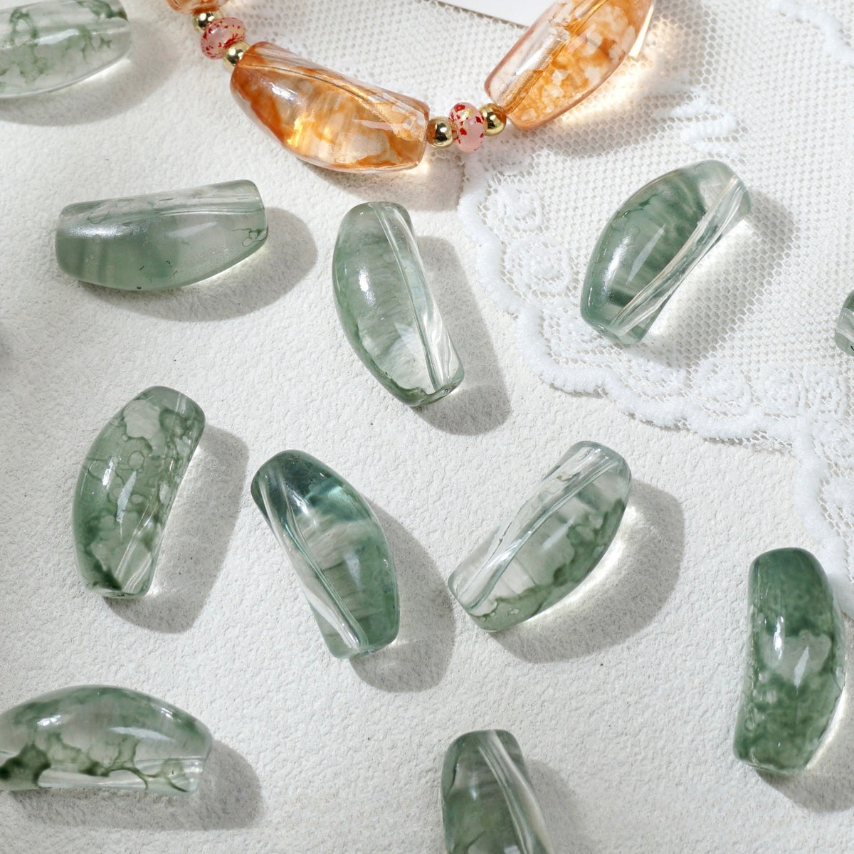 Translucent green marbled curved glass tube beads scattered on white textured fabric