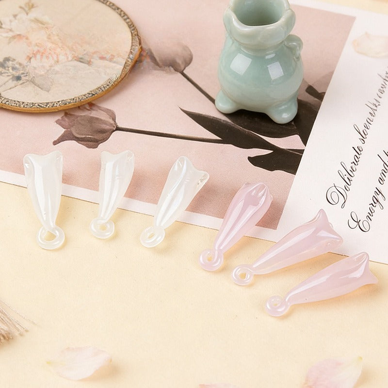 White and pale pink translucent magnolia flower glass pendant beads on cream surface with vase and mirror props