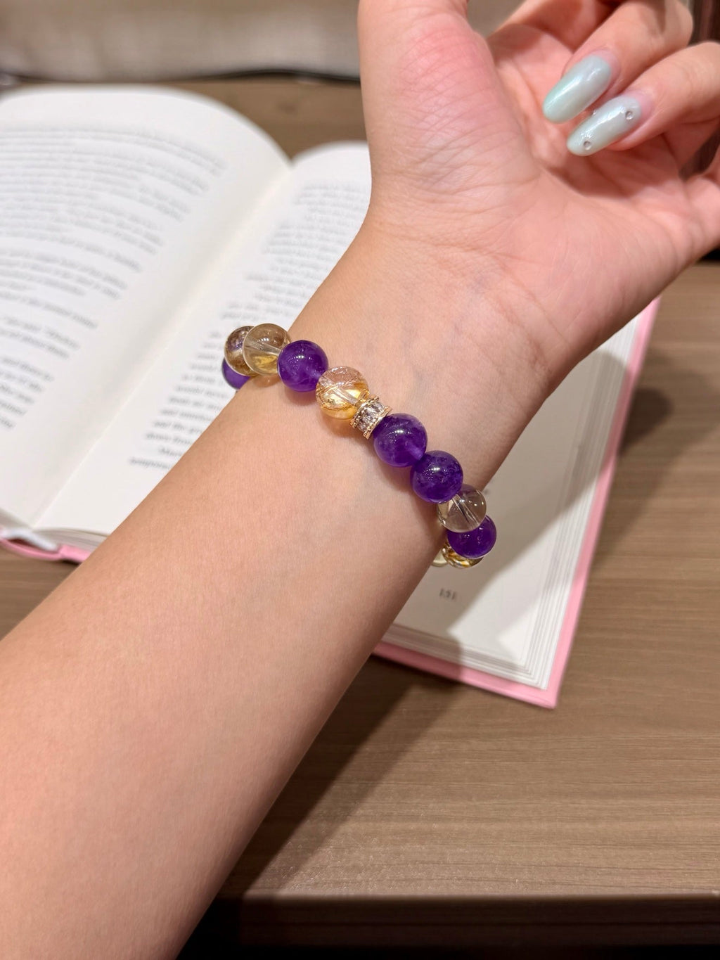 Purple amethyst and gold citrine bracelet worn on wrist over open book