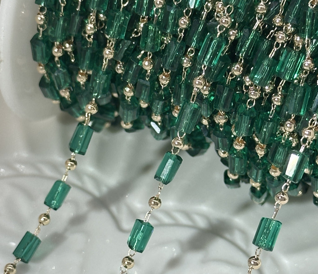 A close-up of a beaded garland featuring translucent green glass beads and small metallic gold-toned spacer beads, draped over a white surface.