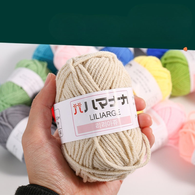 A hand holds a beige skein of yarn with a white paper label that reads 'LILIARG' and Korean text, with other colorful yarn skeins blurred in the background.