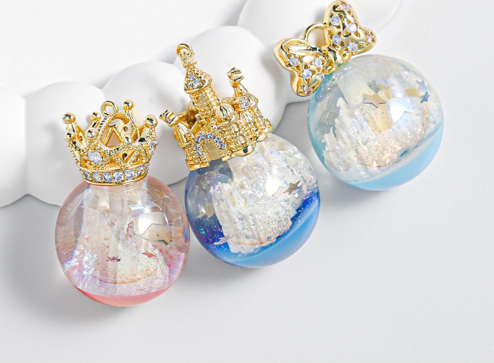 Three transparent resin globe beads with gold crown tops, miniature castle scenes inside, pink, blue, and light blue.