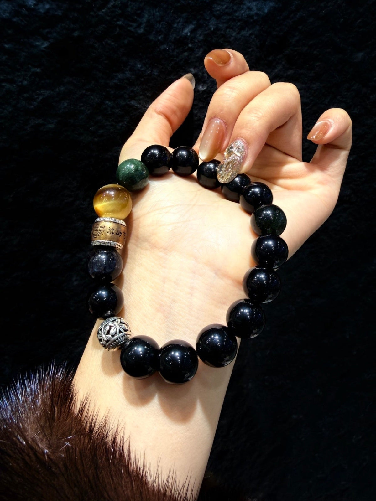 Beaded bracelet on hand with glossy black beads and green, amber, silver and gold accents