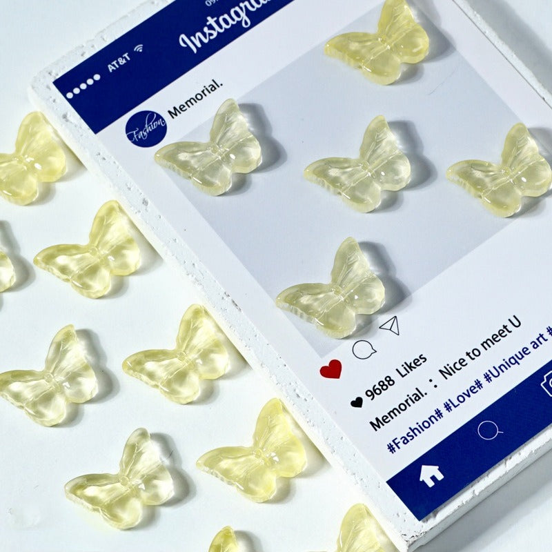 Translucent pale yellow butterfly-shaped glass beads on a white surface next to a printed card