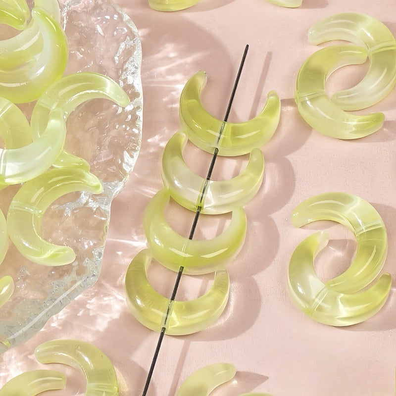 Translucent pale yellow glazed glass crescent moon beads, some strung on a black wire and others on a clear dish