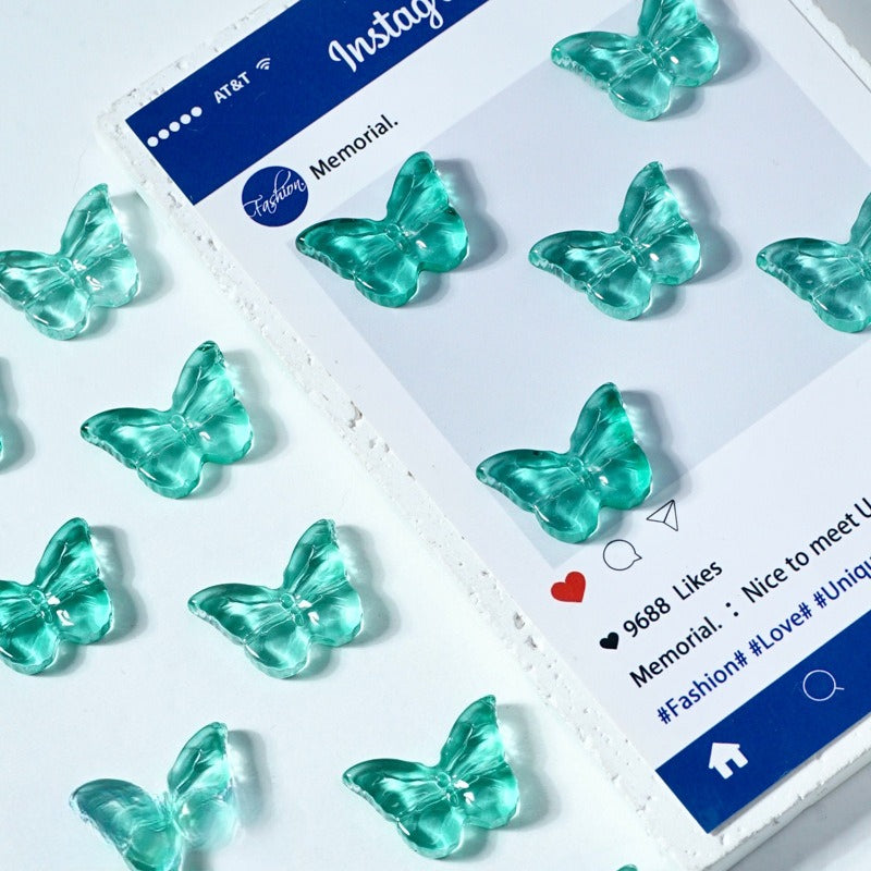 Translucent aqua glass butterfly charms arranged on a white surface next to a printed card