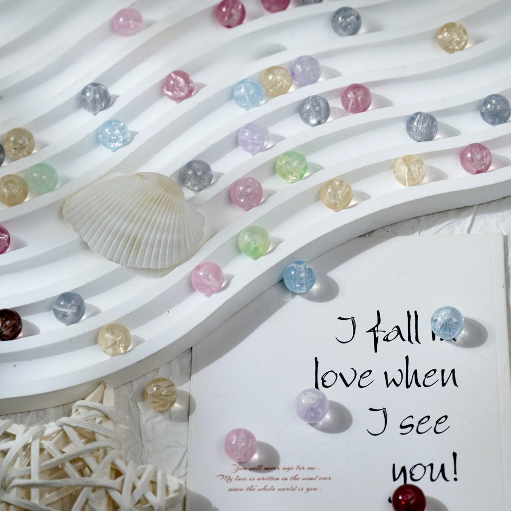 Pastel glass beads on a white wavy display board with a seashell