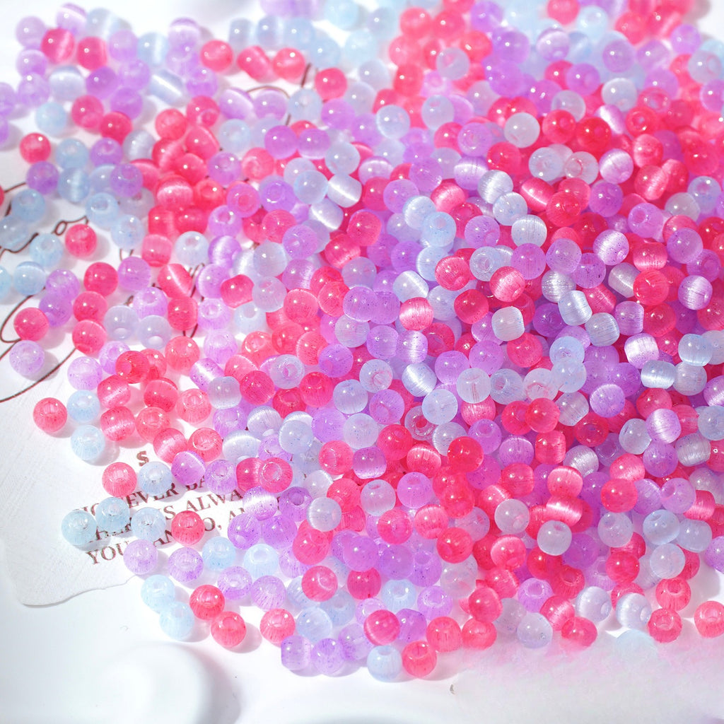 Close-up pile of frosted pink, purple, and pale-blue cat's-eye glass beads on white surface
