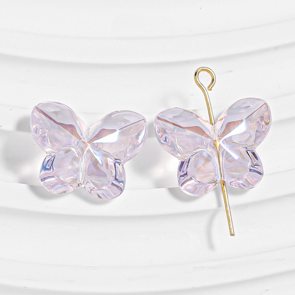 Two iridescent clear butterfly-shaped beads, one threaded on a gold headpin, on a white textured background