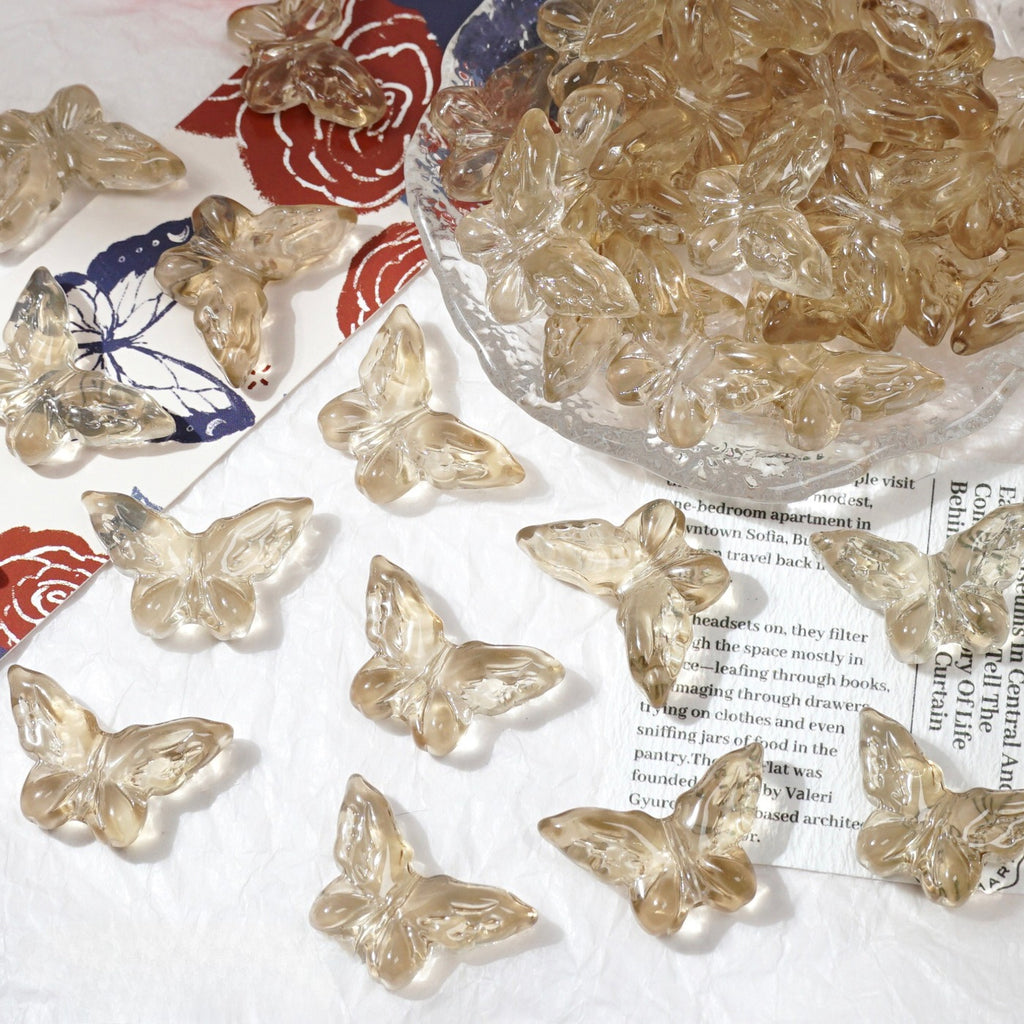 Clear glass butterfly beads scattered on white textured surface with glass bowl