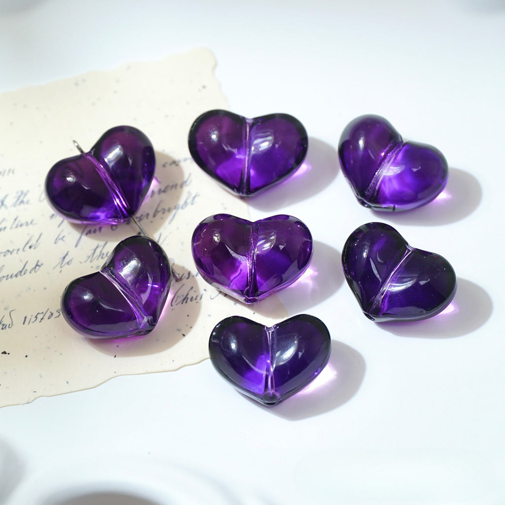 Six translucent purple heart-shaped glass beads on a white surface