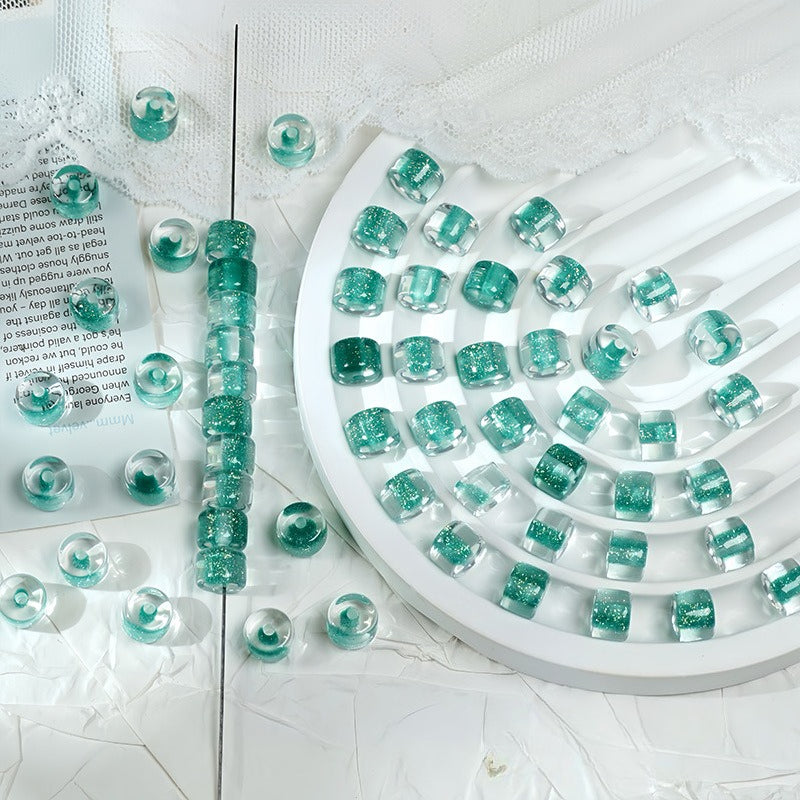 Mint green glitter barrel beads on a white spiral tray with a beaded strand and loose beads on fabric