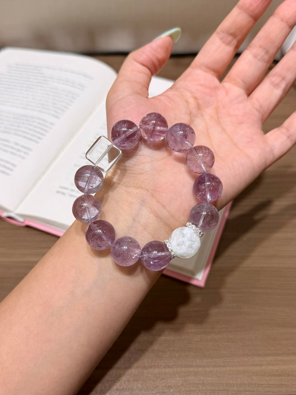 Hand holding purple mist snow bracelet over open book