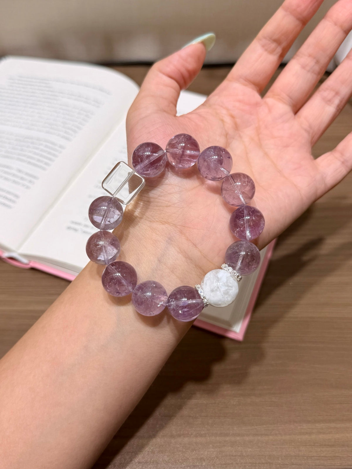 Hand holding purple mist snow bracelet over open book