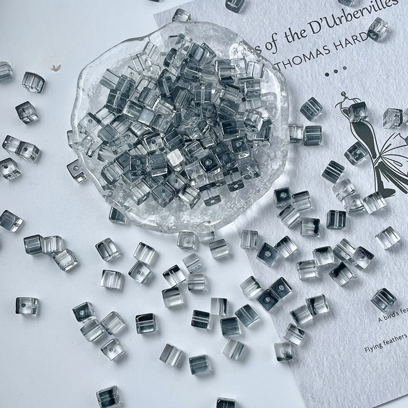 Clear square glass beads scattered on white, glass dish filled with beads