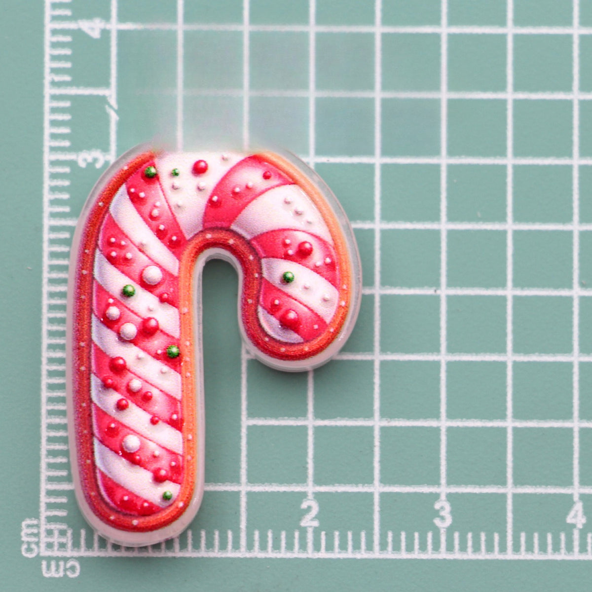 Candy cane acrylic charm with red and white stripes and sprinkles on green gridded cutting mat