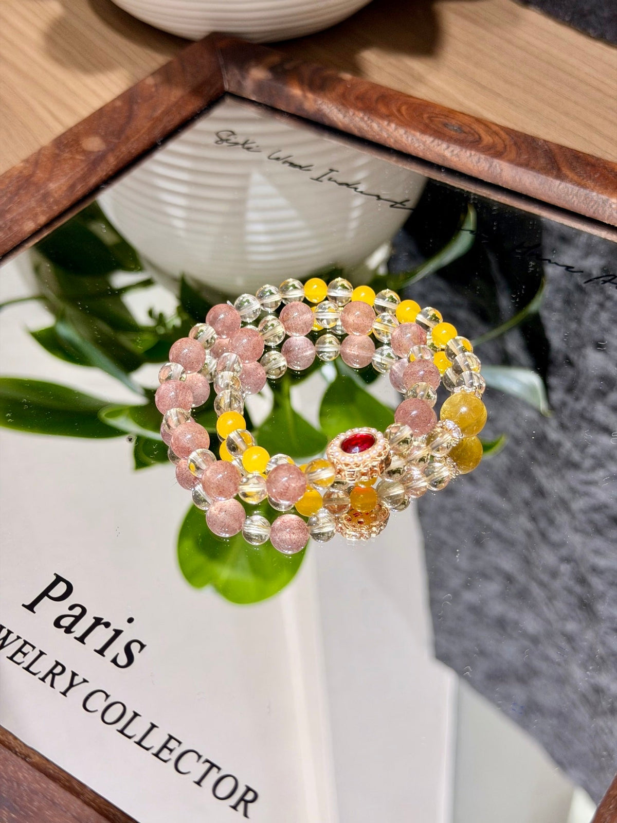 Pink and yellow beaded stretch bracelet with clear faceted beads and a gold charm with red heart-shaped stone on a mirror