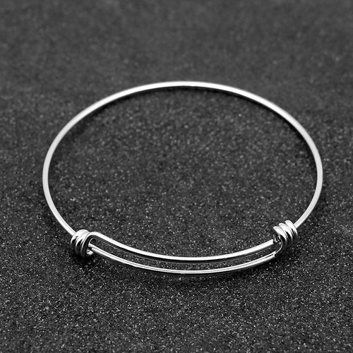A thin silver wire bangle bracelet with decorative spiral wraps at both ends, displayed on a dark textured background.