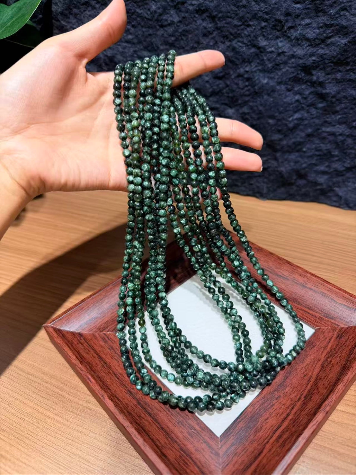 Hand holding multiple strands of Verdant Dragon seraphinite beads, 5.6mm