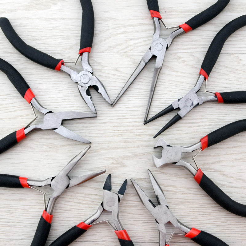 Six pairs of metal wire-nose pliers arranged in a circle on a light wood surface, each with black and red handles.