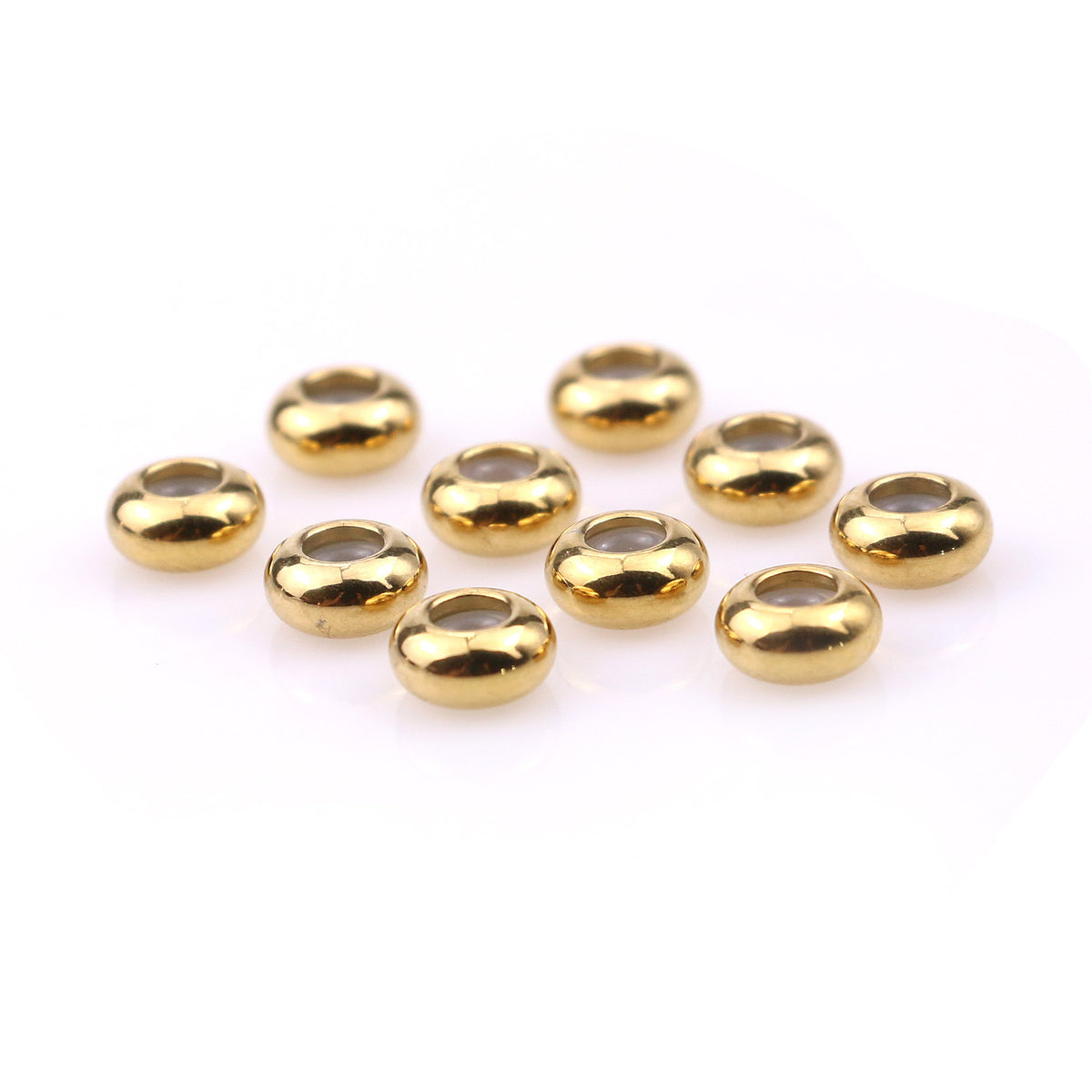 Ten gold stainless steel rounded abacus stopper beads arranged on white, angled view