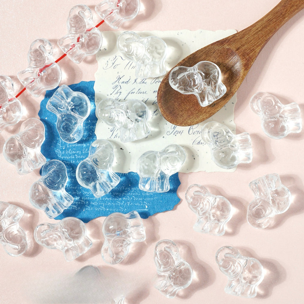 Clear elephant-shaped glass beads on pink with a wooden spoon, blue paper and handwritten notes