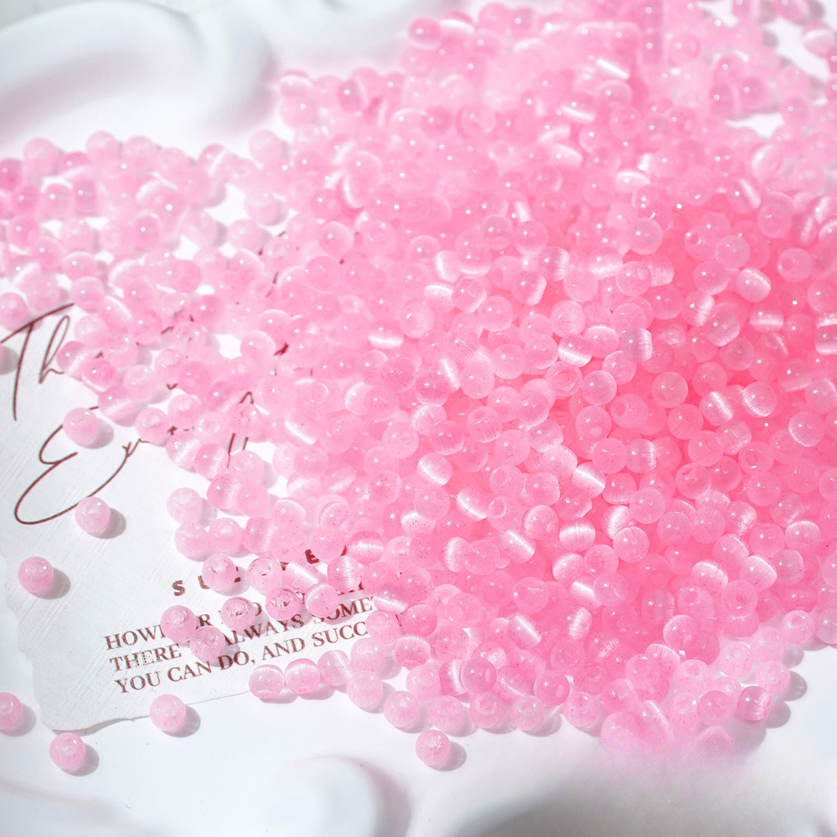 Close-up pile of frosted pink cat's-eye glass beads on white surface