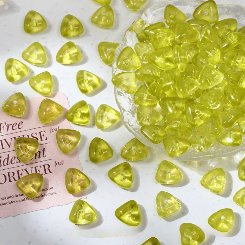 Yellow translucent triangle-shaped glass beads scattered on white with a clear bowl of beads