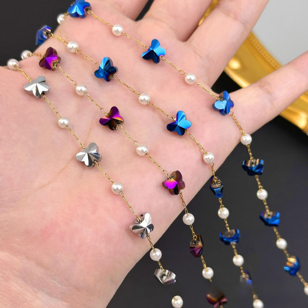 Hand holding gold chain strands with white pearls and iridescent blue, purple, silver butterfly charms