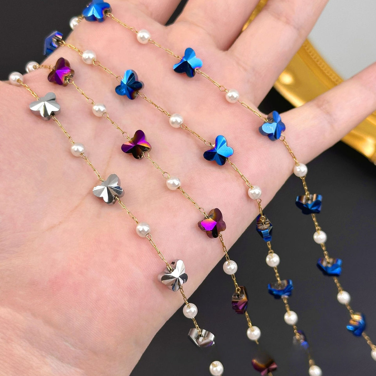 Hand holding gold chain strands with white pearls and iridescent blue, purple, silver butterfly charms