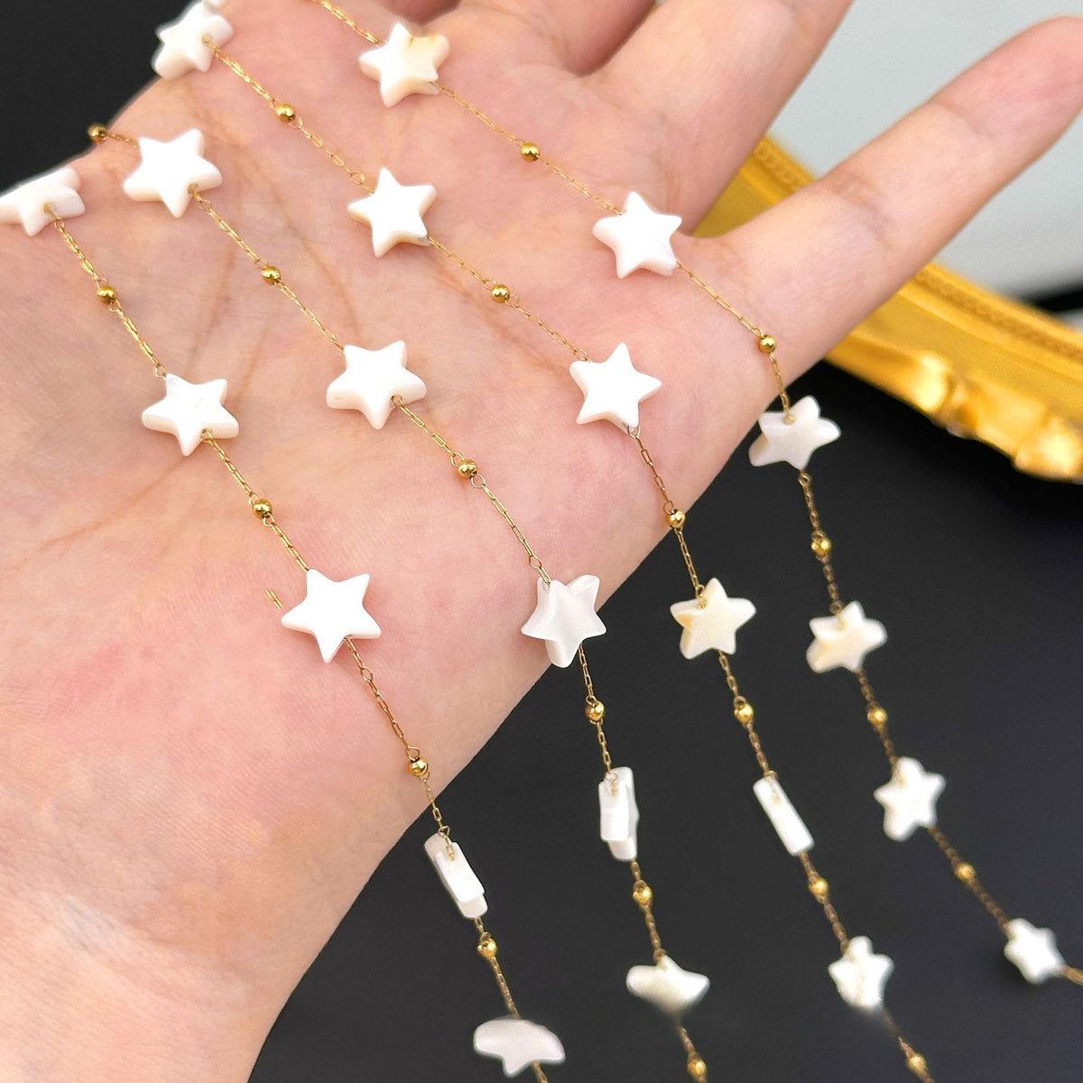Hand holding strands of 18K gold-plated chain with white star beads and small gold spacer beads