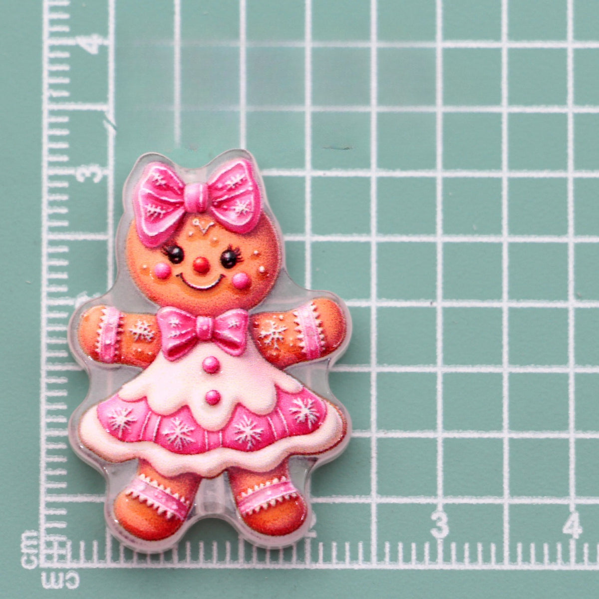 Gingerbread doll acrylic charm with pink bow and dress on green gridded measuring surface