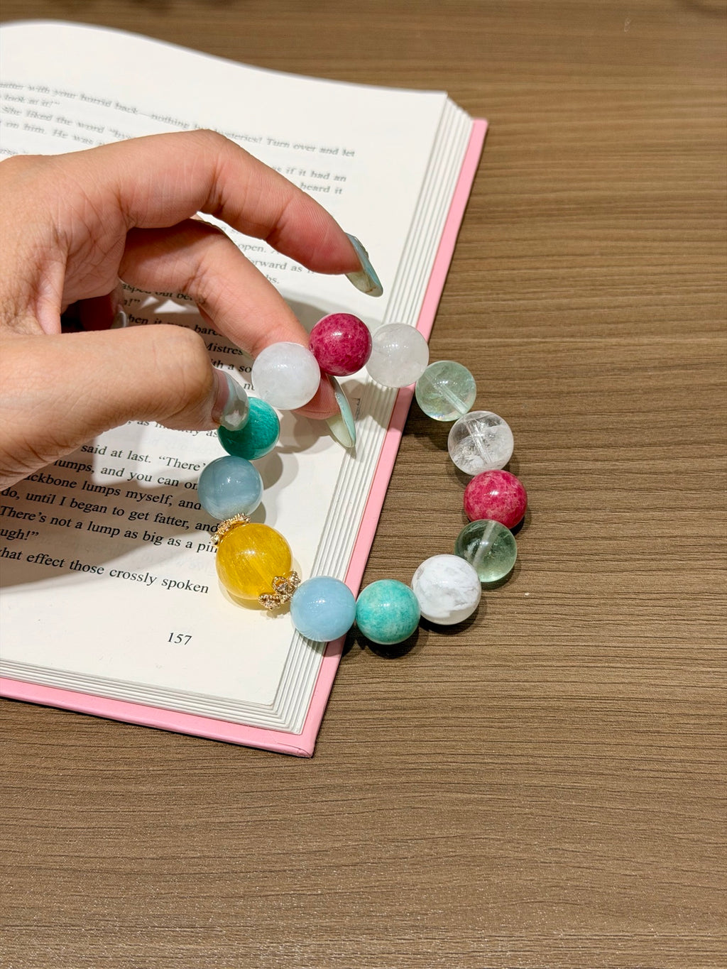 Hand holding the Woven Sea Reverie bracelet over an open book
