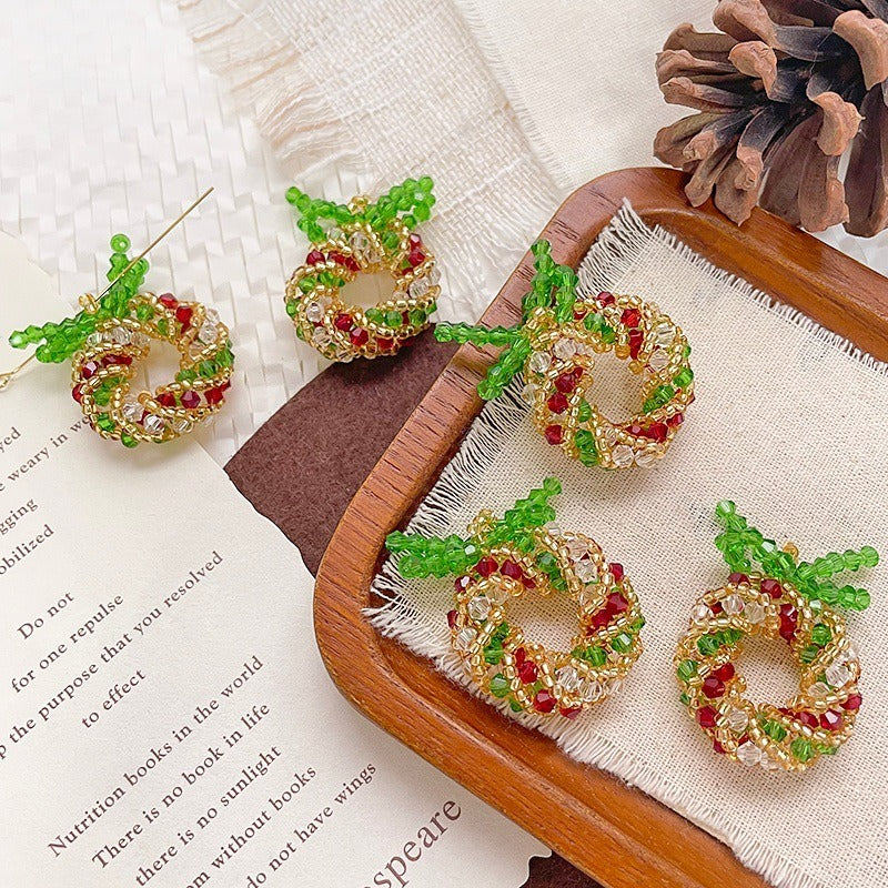 Small beaded Christmas wreath ornaments with green bows in red, gold, and green seed beads on a wooden tray