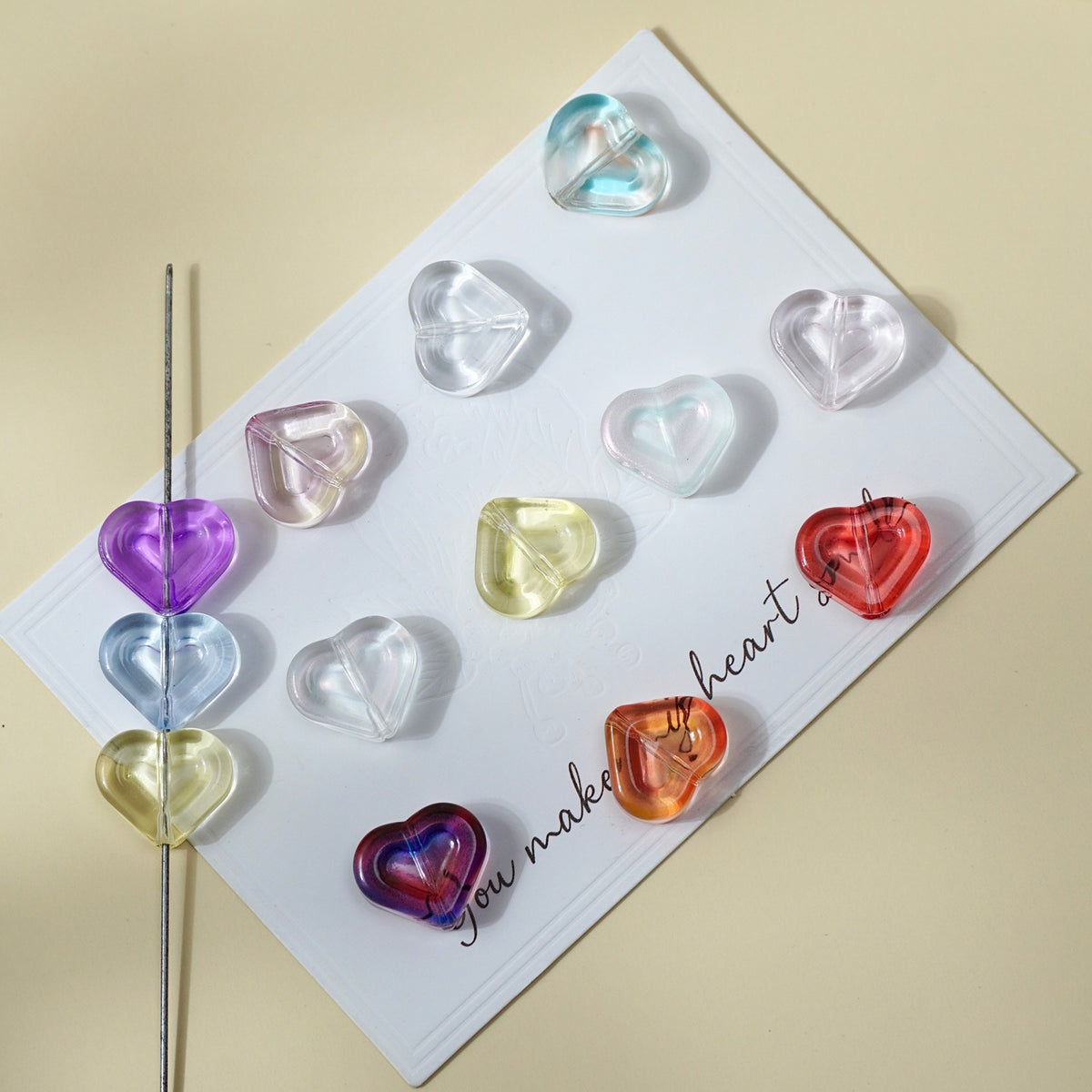 Translucent heart-shaped double-layer glass beads in purple, blue, pink, yellow, orange and red on a white card