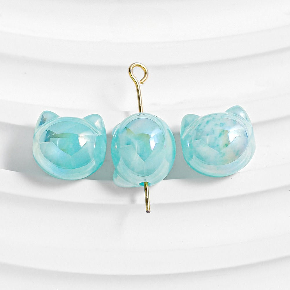 Three light blue cat-shaped beads with faceted details and gold metal loops on a white background.