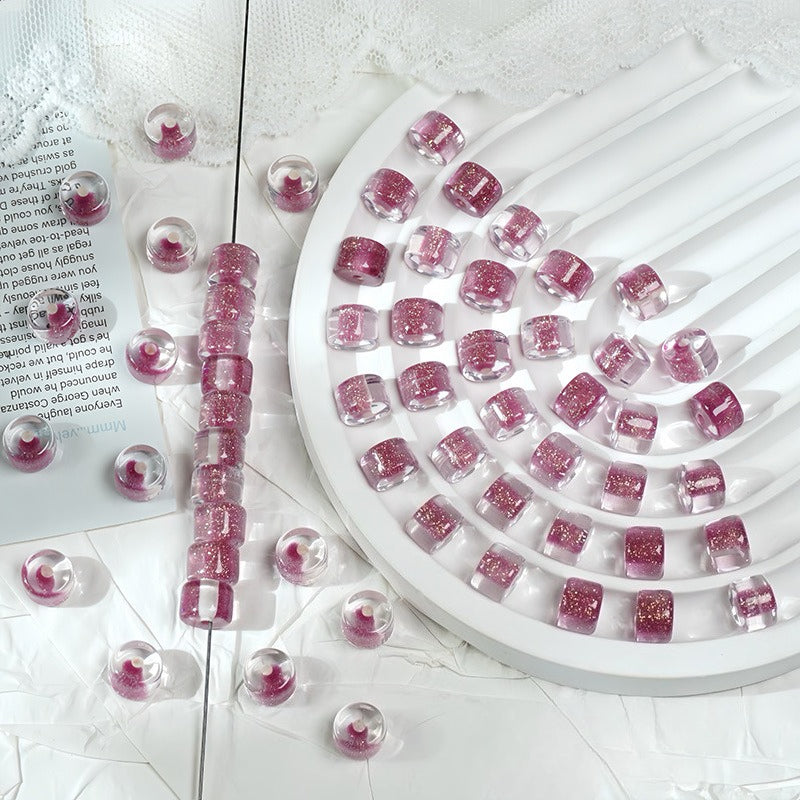Dark pink glitter barrel beads on a white spiral tray with a beaded strand and loose beads scattered
