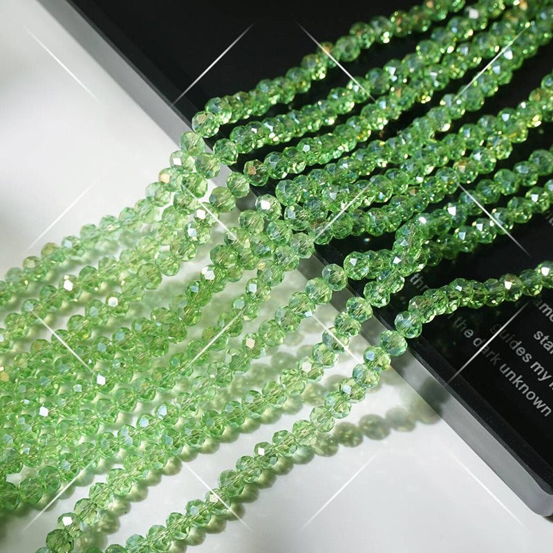 Strands of green faceted crystal glass wheel beads arranged diagonally on white surface