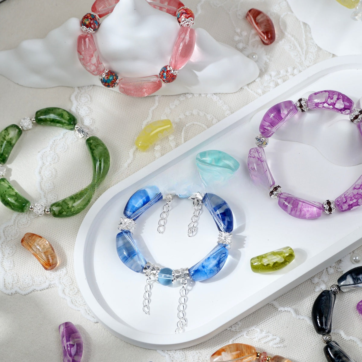 Bracelets made with pink, green, blue, and purple curved glass tube beads with flower patterns, styled on a white tray
