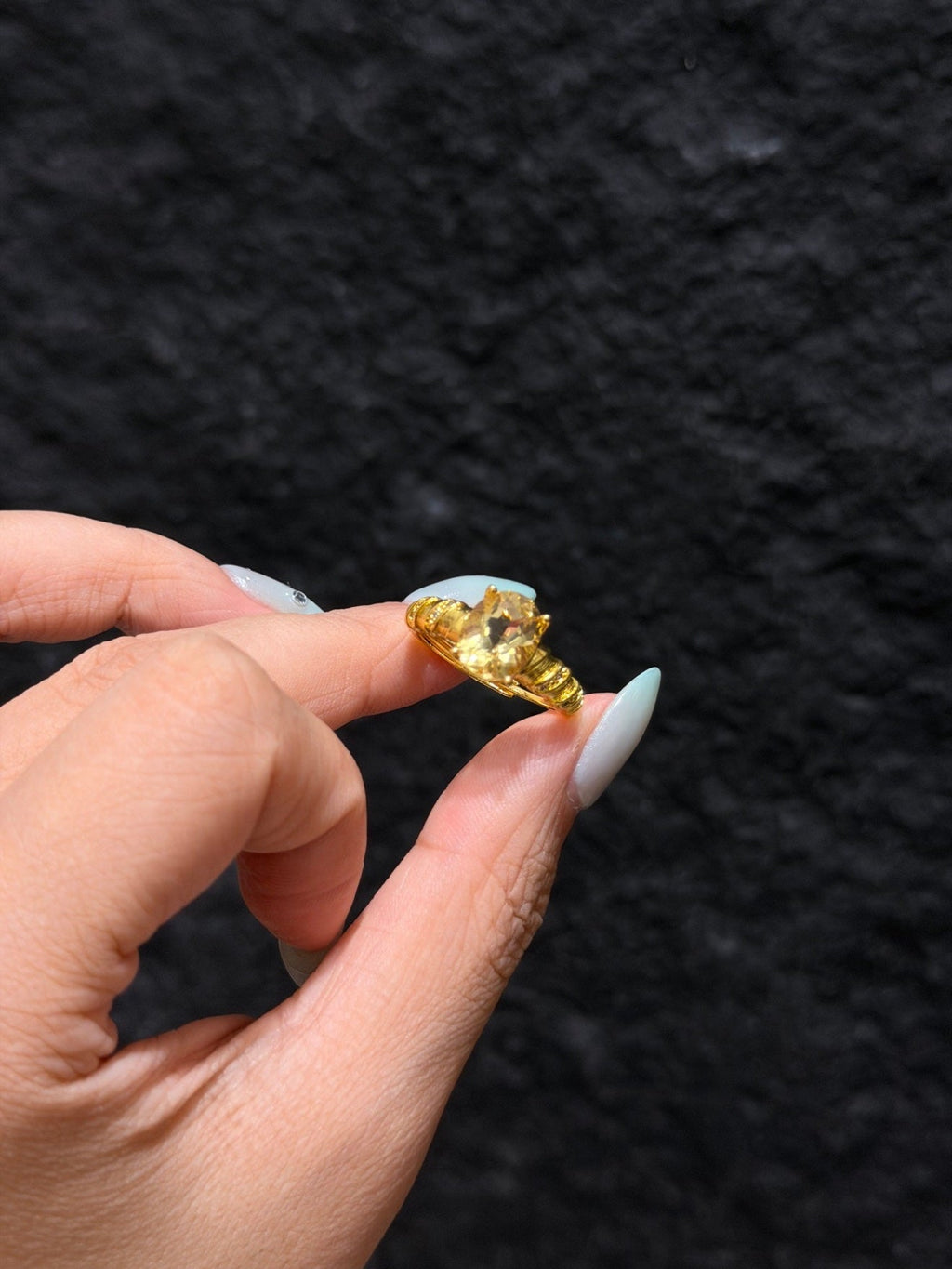 Hand with blue nails holding a golden citrine solitaire ring