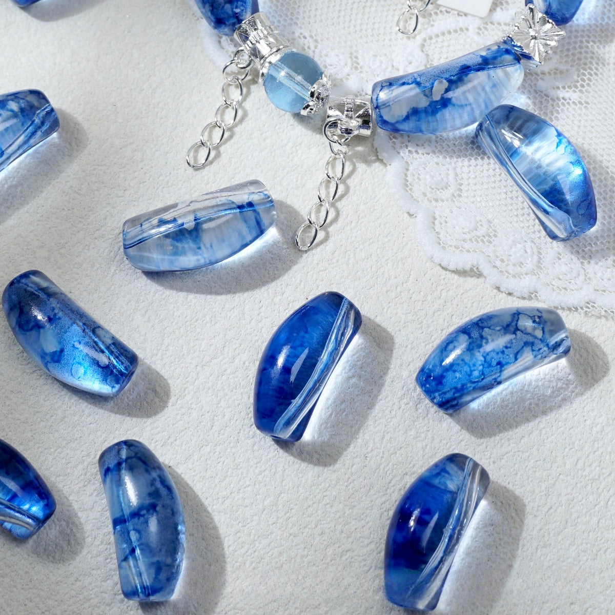 Blue marbled glass beads with silver chain extender clips, arranged on a textured white fabric background.