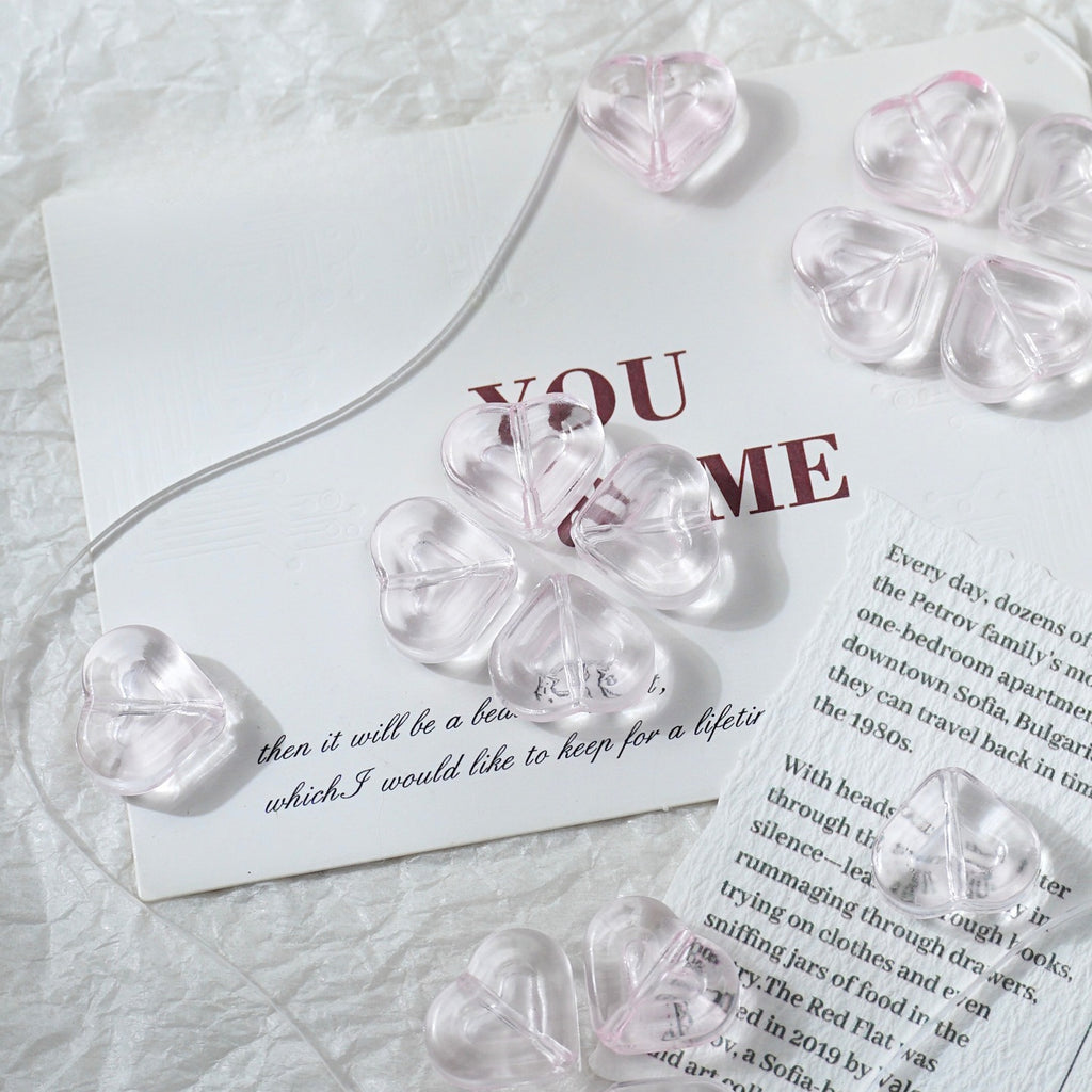 Clear heart-shaped glass beads threaded on a transparent string, arranged on white textured paper with printed text.