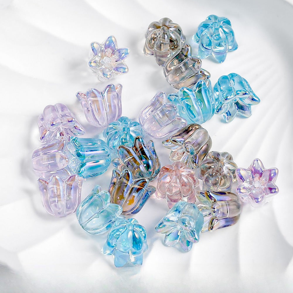 A pile of small translucent lily-shaped glitter beads in pastel blue, lavender, pink and iridescent tones on white fabric