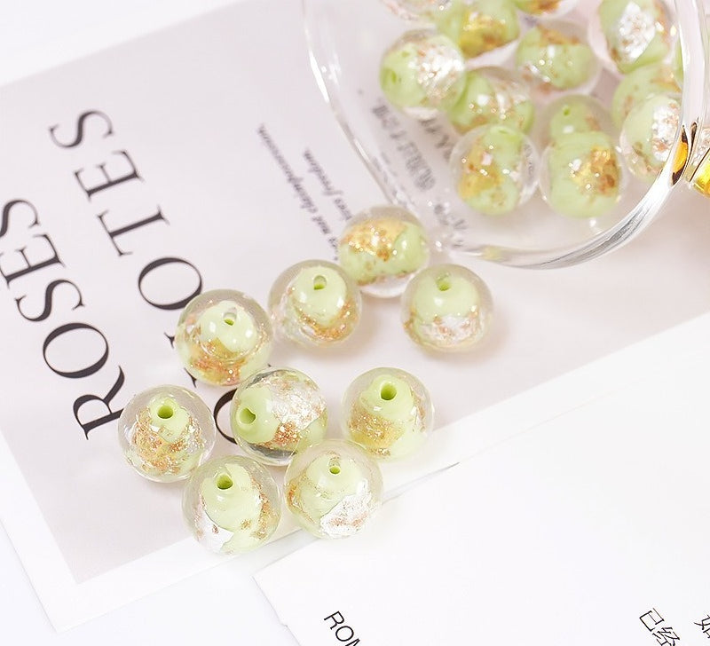 Pale green and gold-foil glass beads scattered on a printed card beside a glass bowl