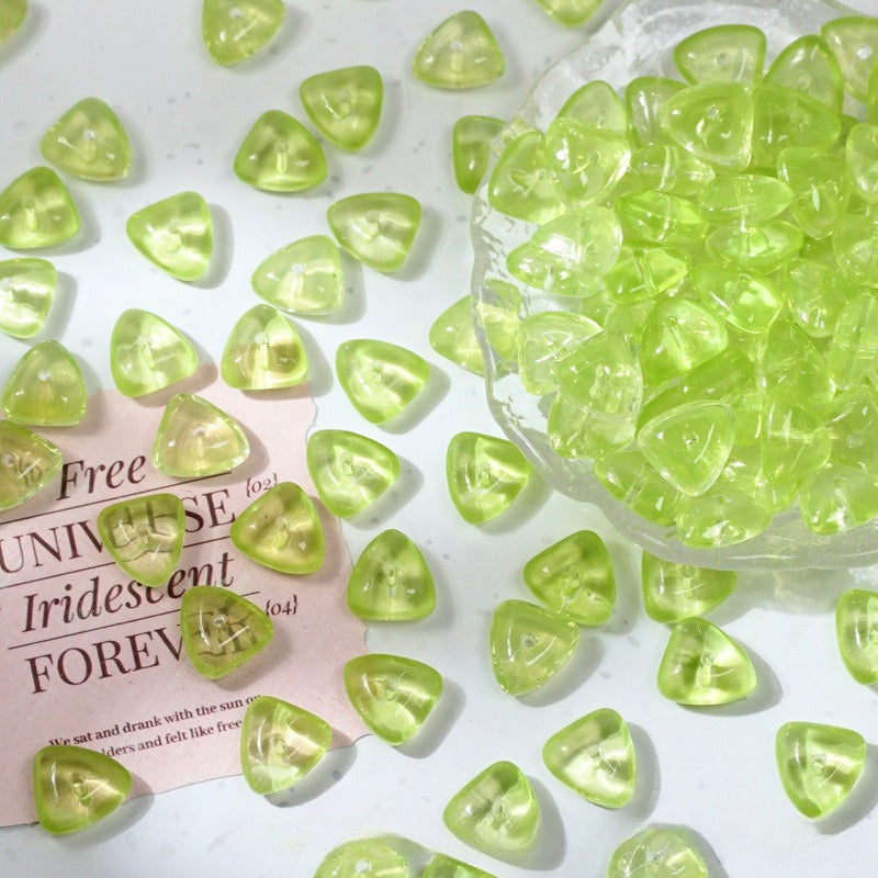 Iridescent lime green glass beads shaped like small teardrops scattered on a white surface