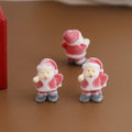 Three small Santa Claus figurines with frosted candy-coated texture standing on brown surface