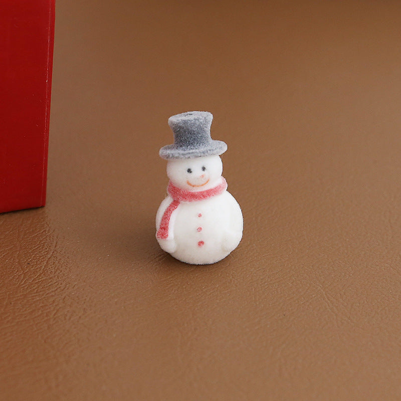 Small white snowman figurine with gray top hat and pink scarf standing on brown textured surface