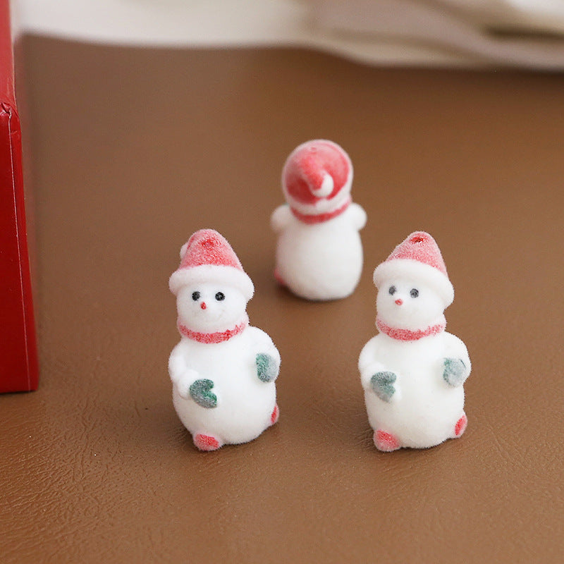 Three small white snowman figurines with red hats and scarves plus two green mittens
