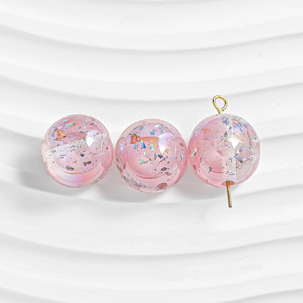 Three pink glitter resin beads on white; right bead has gold loop and pin