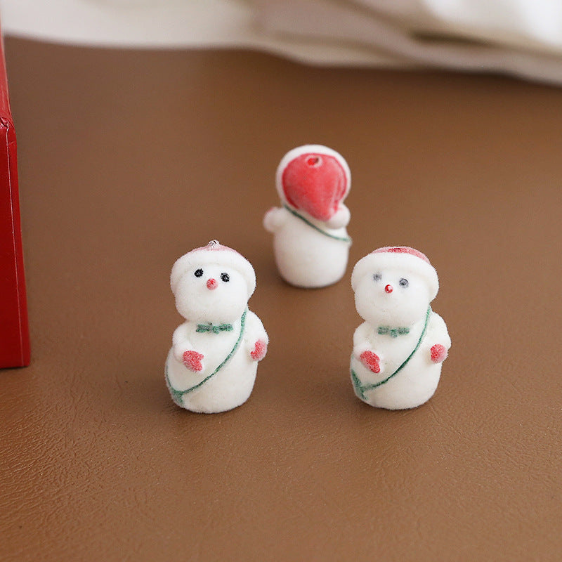 Three small white snowman figurines with red and green holiday details arranged on brown surface